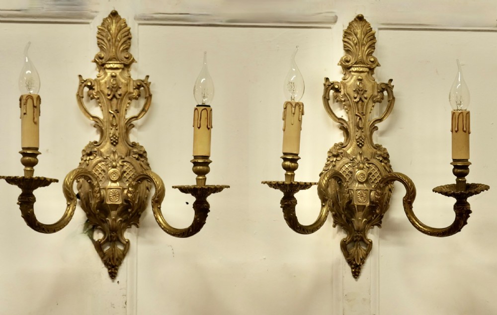 A pair of ornate cast brass twin-arm wall sconces featuring Rococo scrollwork and faux candle drip sleeves. View IV