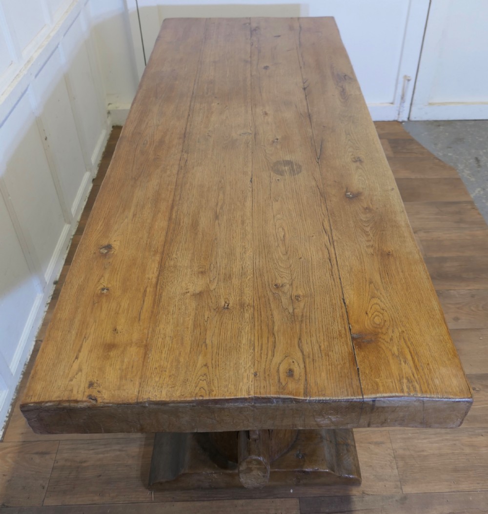 A 19th-century French oak refectory table featuring a thick rectangular top supported by heavy cylindrical pedestal legs connected by a central stretcher. View XII