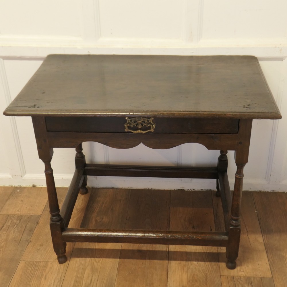 An eighteenth-century dark oak lowboy table featuring a single drawer with a brass handle, a shaped lower apron, turned legs, and a perimeter stretcher. View II