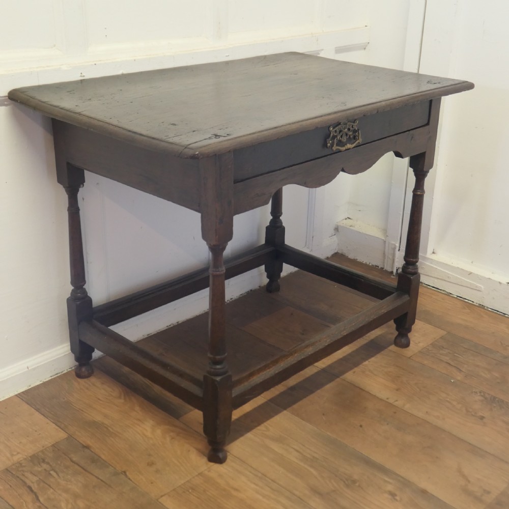 An eighteenth-century dark oak lowboy table featuring a single drawer with a brass handle, a shaped lower apron, turned legs, and a perimeter stretcher. View V