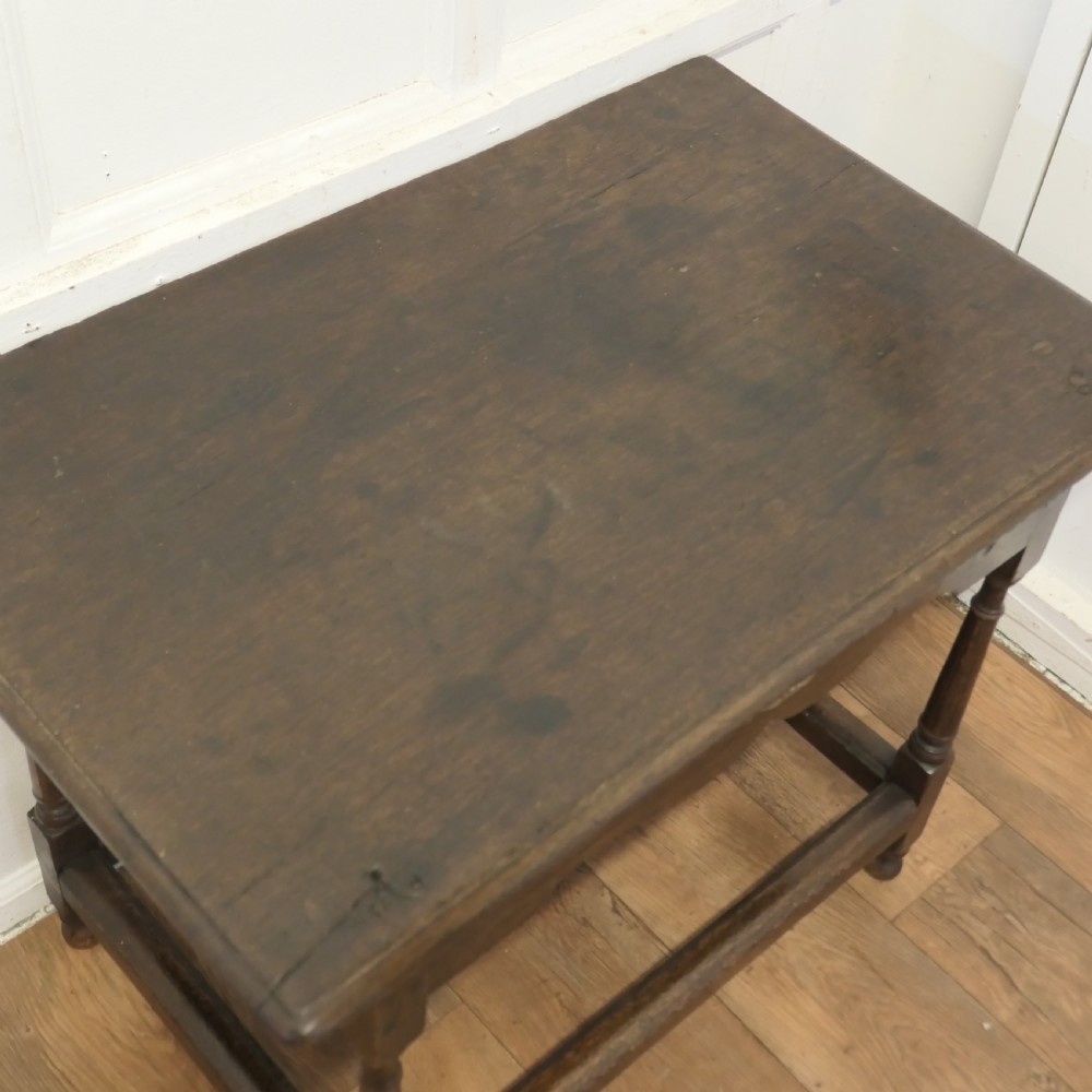 An eighteenth-century dark oak lowboy table featuring a single drawer with a brass handle, a shaped lower apron, turned legs, and a perimeter stretcher. View VI