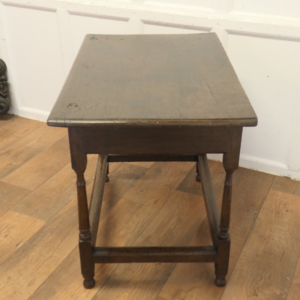 An eighteenth-century dark oak lowboy table featuring a single drawer with a brass handle, a shaped lower apron, turned legs, and a perimeter stretcher. View VII