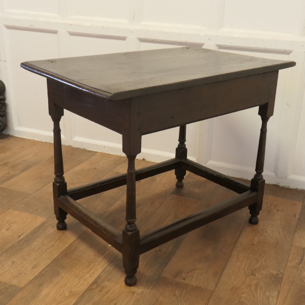 An eighteenth-century dark oak lowboy table featuring a single drawer with a brass handle, a shaped lower apron, turned legs, and a perimeter stretcher. View VIII