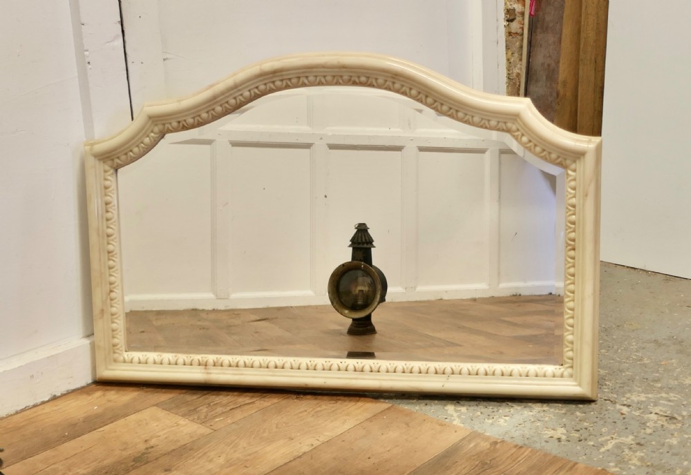 A large arched overmantel mirror featuring a cream simulated marble finish and carved egg-and-dart moulding along the interior rim.