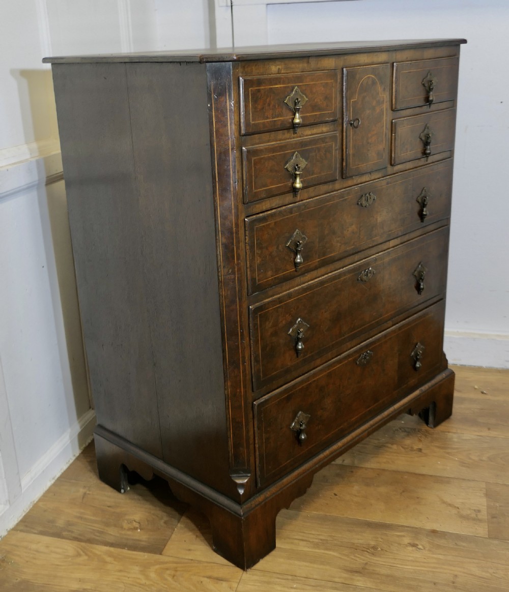 A tall burr walnut chest of drawers featuring a central arched cupboard door, crossbanded drawer fronts, brass drop handles, and bracket feet. View III