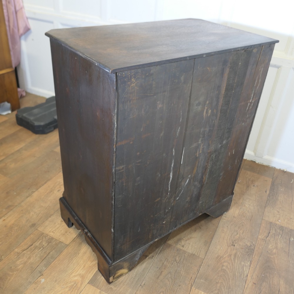 A tall burr walnut chest of drawers featuring a central arched cupboard door, crossbanded drawer fronts, brass drop handles, and bracket feet. View IX