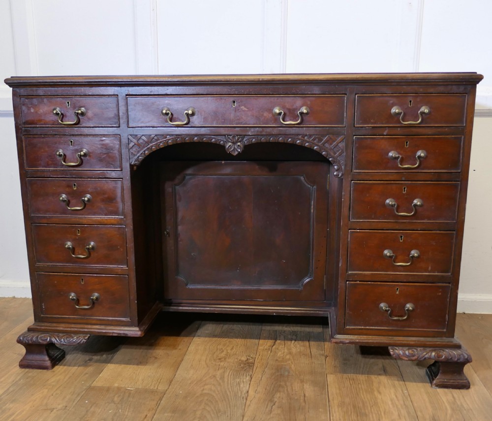 A large dark walnut Victorian kneehole desk featuring ten drawers with brass handles, a central recessed cupboard, and carved feet.