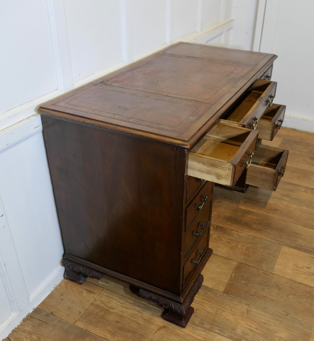 A large dark walnut Victorian kneehole desk featuring ten drawers with brass handles, a central recessed cupboard, and carved feet. View V