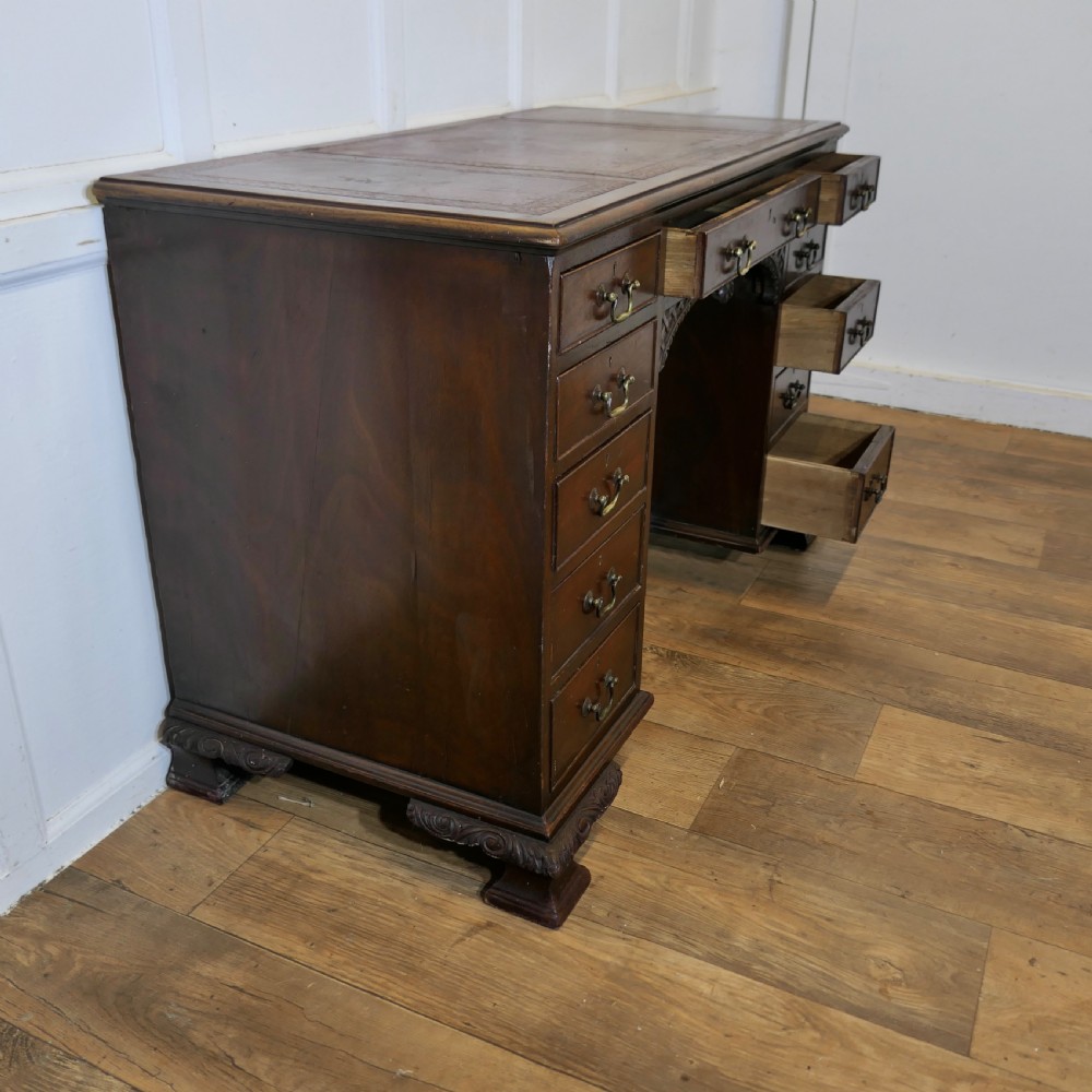 A large dark walnut Victorian kneehole desk featuring ten drawers with brass handles, a central recessed cupboard, and carved feet. View X