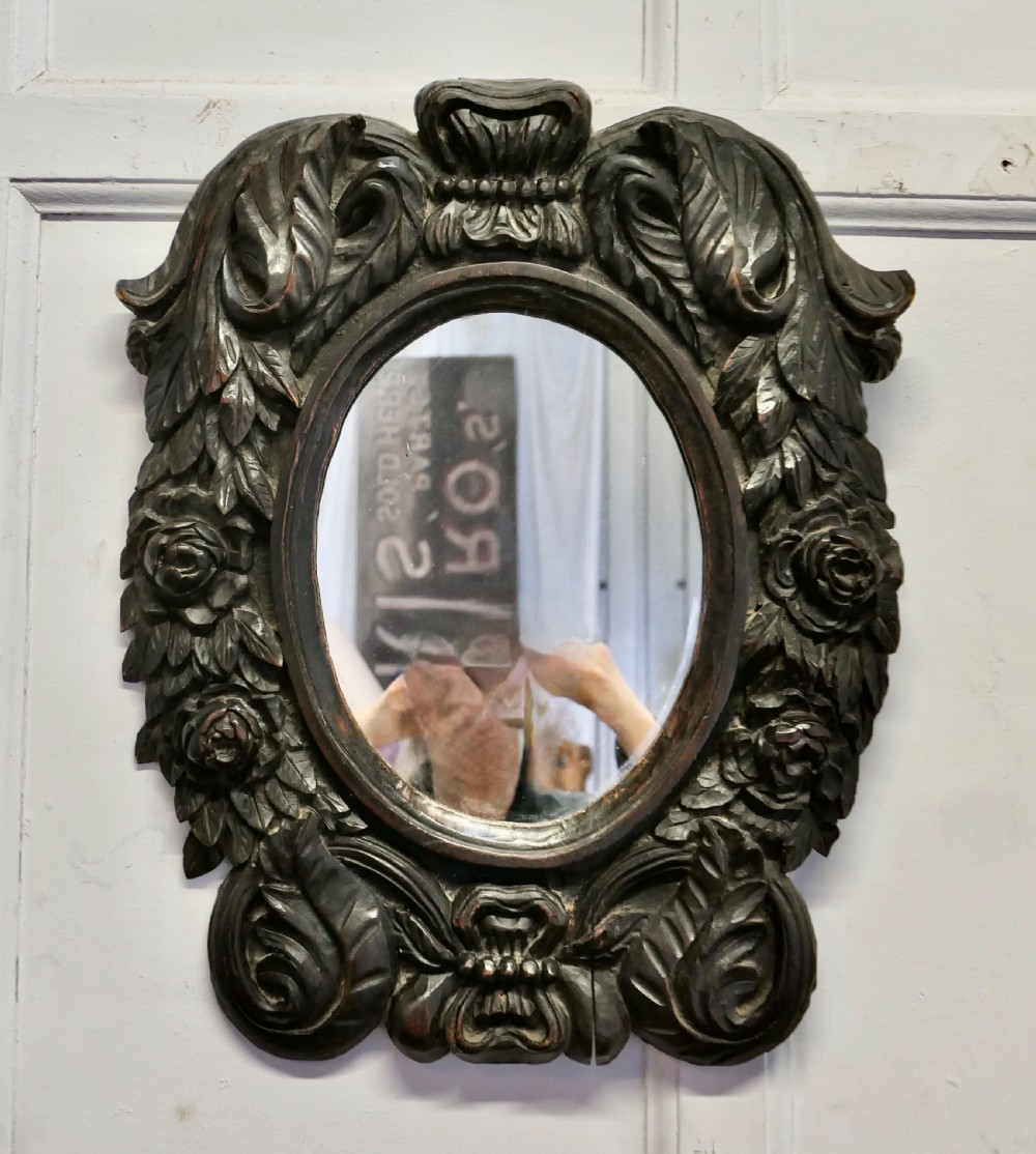 An oval glass mirror enclosed within a deeply carved dark oak frame featuring floral and leaf relief details. View II