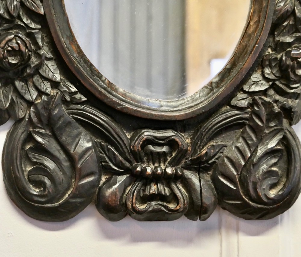 An oval glass mirror enclosed within a deeply carved dark oak frame featuring floral and leaf relief details. View IV