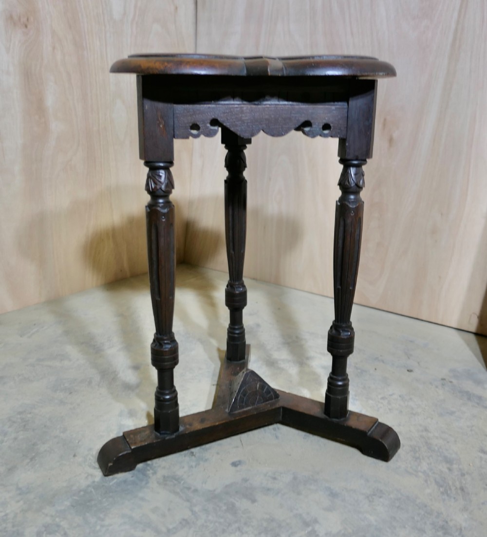 A dark carved oak occasional table featuring a clover-shaped top, scalloped apron, three fluted turned legs, and a tripod base. View V
