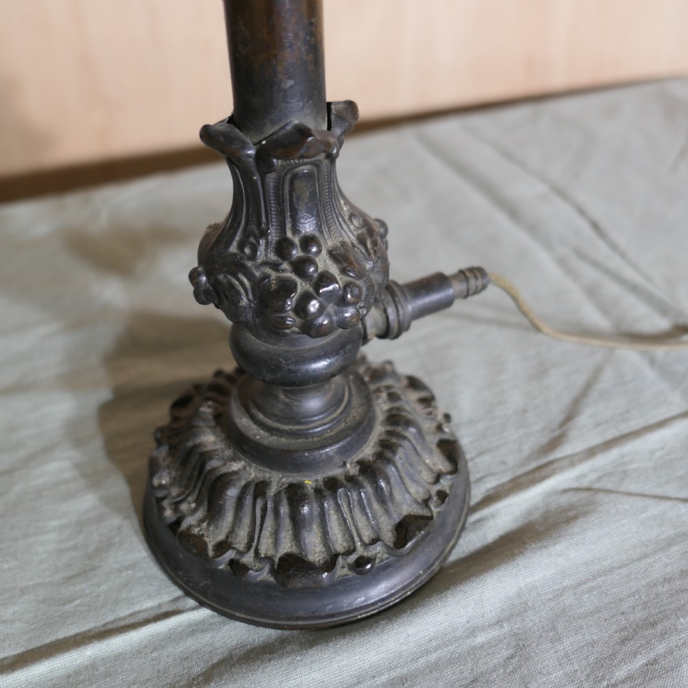 A Victorian dark bronze table lamp featuring a cast ornate base, a turned stem, and an illuminated diamond cut glass shade. View VII