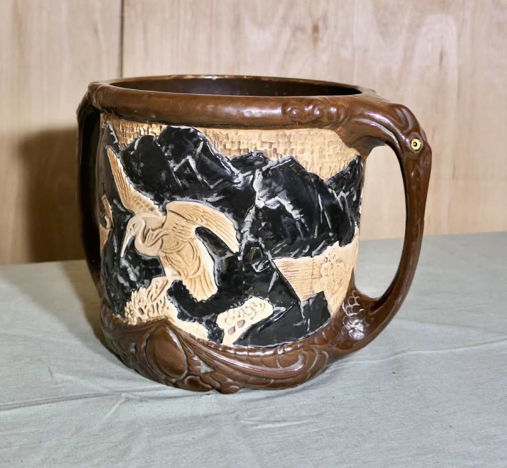 A cylindrical Bretby earthenware jardiniere featuring dark brown glazed twin handles and a cream central band decorated with relief-carved Japanese figures. View V