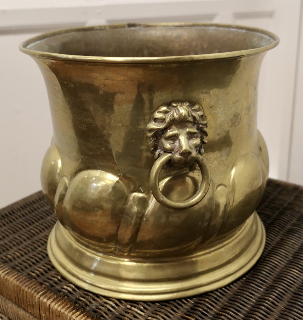 A large round brass jardiniere with gadrooned lower relief, flared upper rim, stepped base, and cast lion mask handles holding drop rings. View III