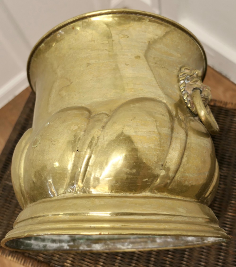 A large round brass jardiniere with gadrooned lower relief, flared upper rim, stepped base, and cast lion mask handles holding drop rings. View IV