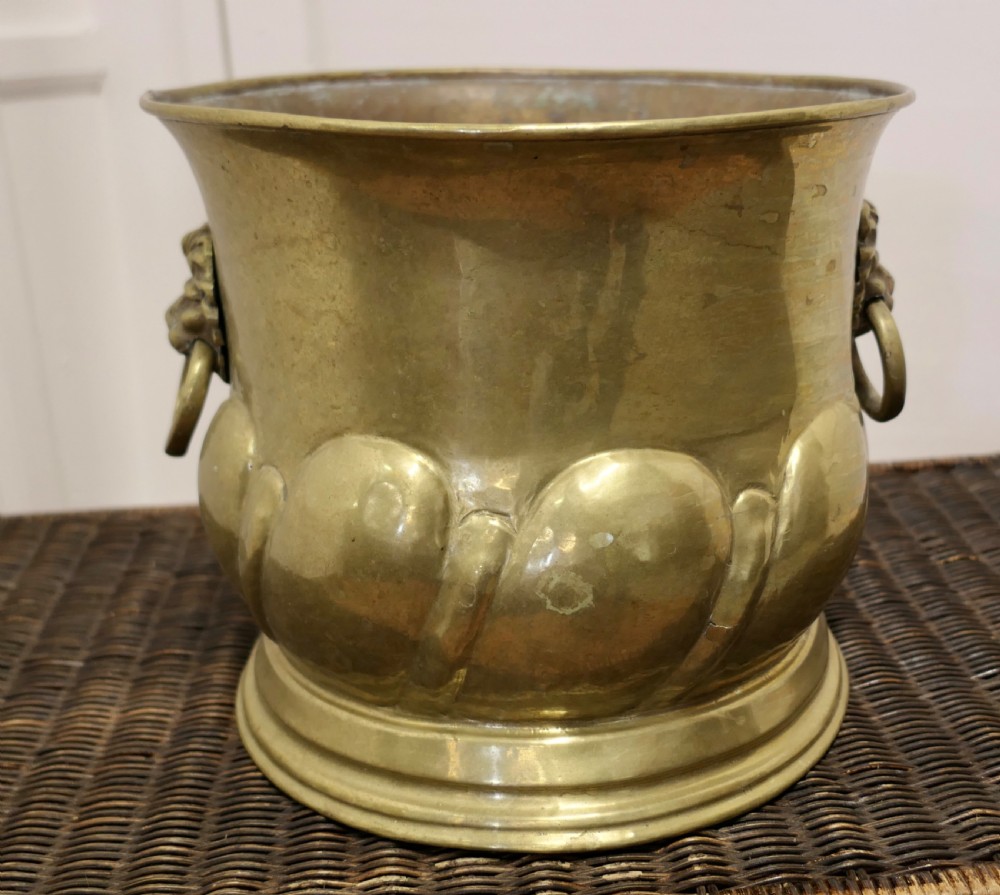 A large round brass jardiniere with gadrooned lower relief, flared upper rim, stepped base, and cast lion mask handles holding drop rings. View V