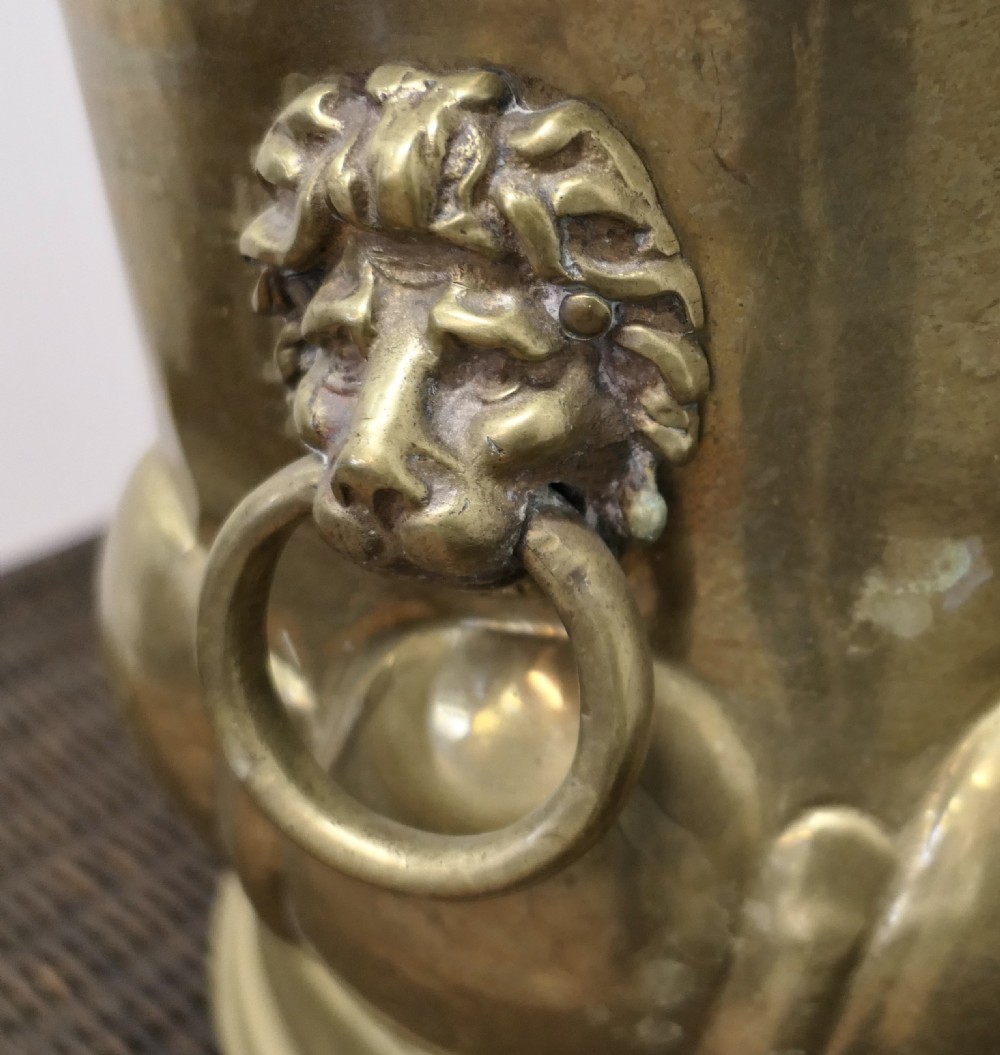 A large round brass jardiniere with gadrooned lower relief, flared upper rim, stepped base, and cast lion mask handles holding drop rings. View VI