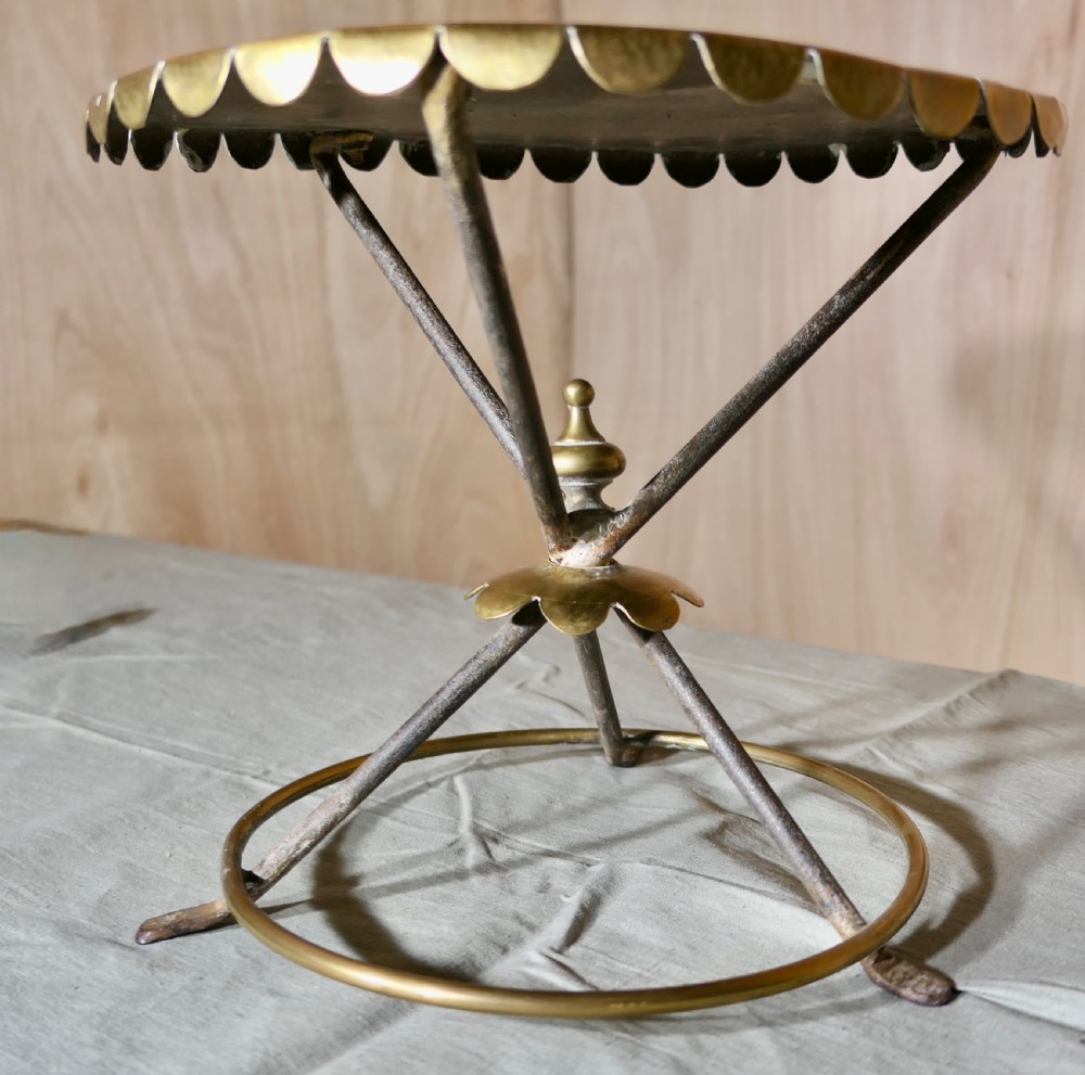 An antique brass and iron gypsy trivet featuring a scalloped brass top plate supported by crossed iron legs and a circular brass base. View VI