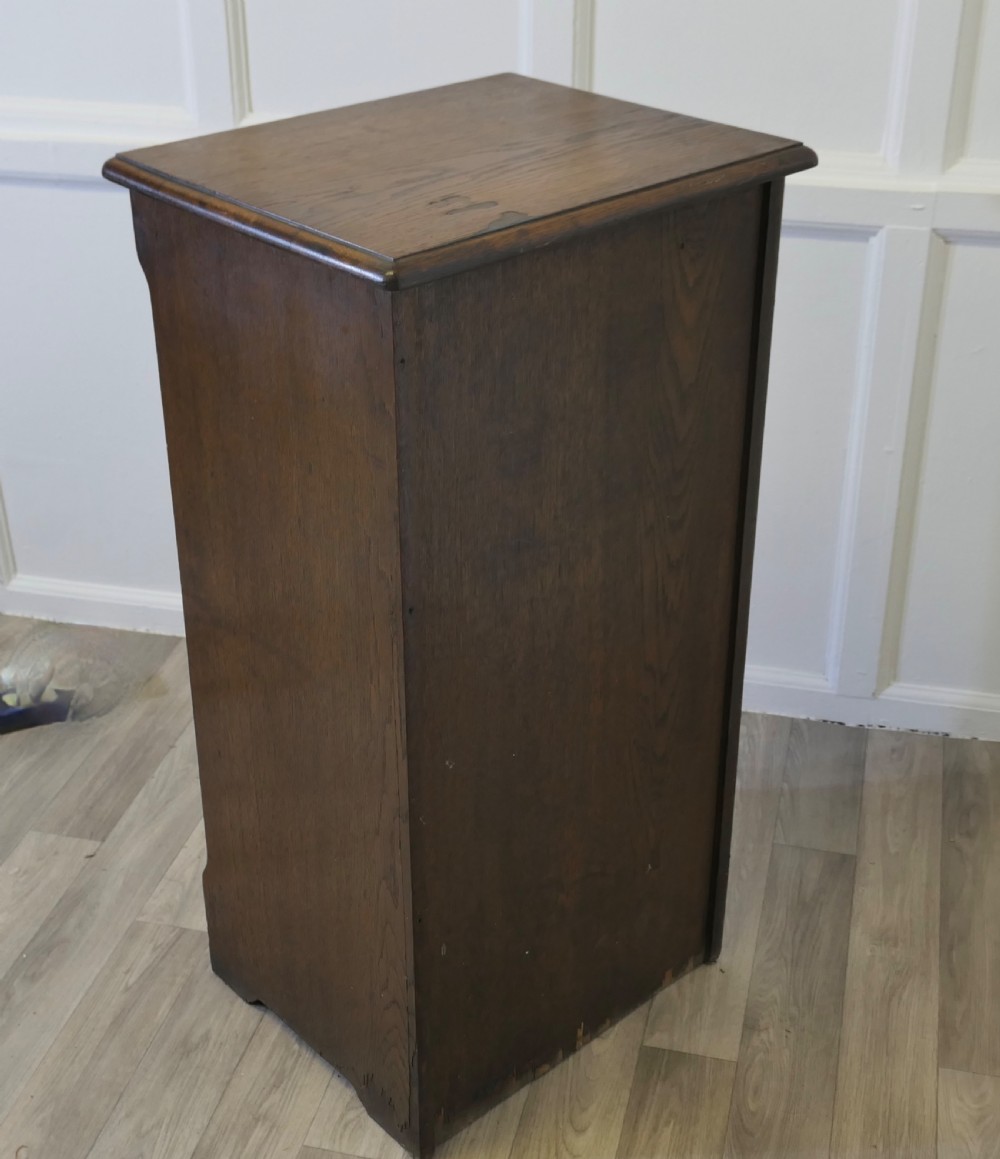 A tall medium brown oak filing cabinet featuring a flexible slatted tambour front, top keyhole escutcheon plate, and a solid plinth base. View VI