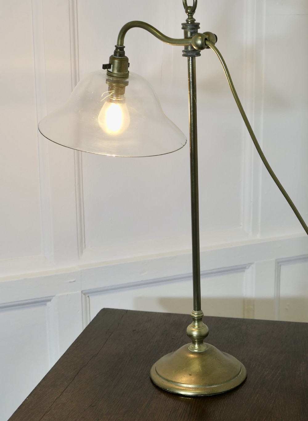 A French brass desk lamp featuring a circular stepped base, an adjustable stem, and a bell-shaped clear glass shade. View V