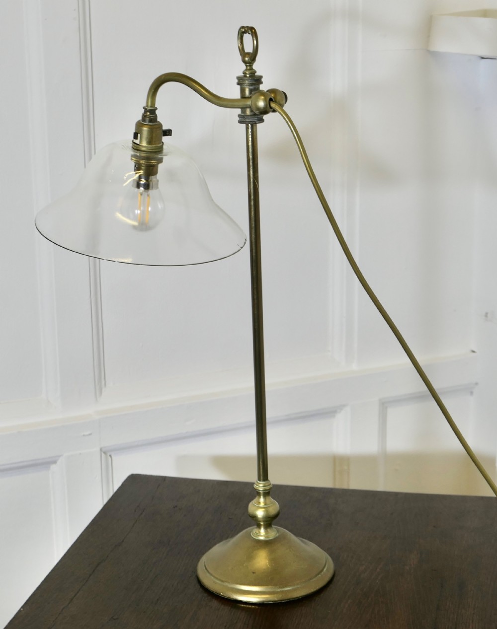 A French brass desk lamp featuring a circular stepped base, an adjustable stem, and a bell-shaped clear glass shade. View VI