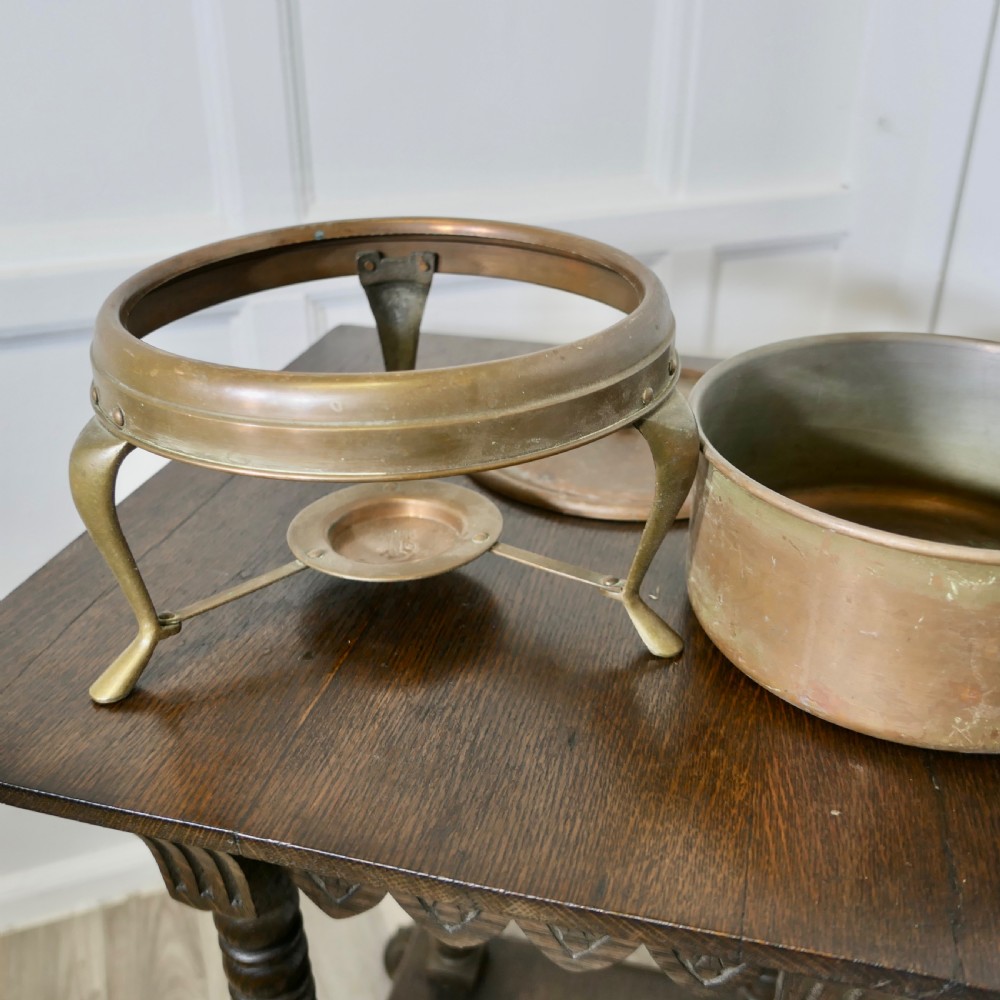 A vintage circular copper bain marie featuring a lid, long handle, and a three-legged brass tripod stand with an integrated burner tray. View III