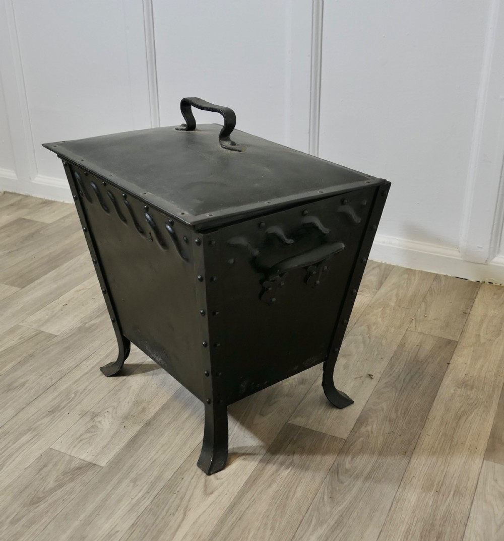 A black riveted metal Arts and Crafts coal box featuring a domed lid with a central handle, decorative wave detailing, and splayed metal legs. View III
