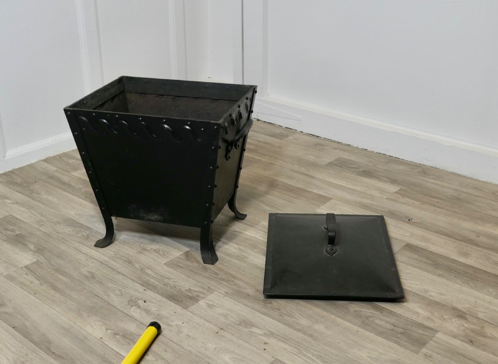 A black riveted metal Arts and Crafts coal box featuring a domed lid with a central handle, decorative wave detailing, and splayed metal legs. View VII