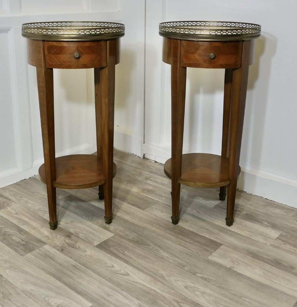 A pair of tall French circular side tables crafted from wood veneer with chevron parquetry drawers, lower shelves, and pierced brass gallery rims.