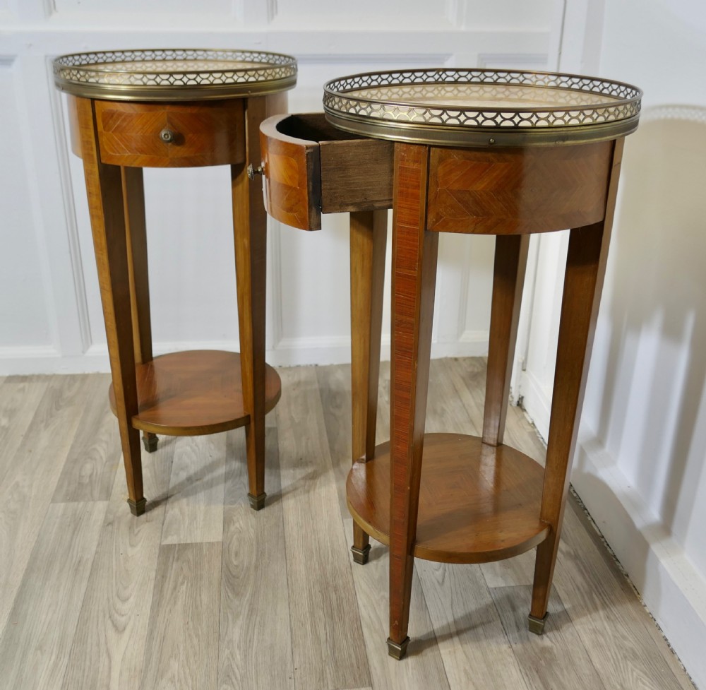 A pair of tall French circular side tables crafted from wood veneer with chevron parquetry drawers, lower shelves, and pierced brass gallery rims. View V