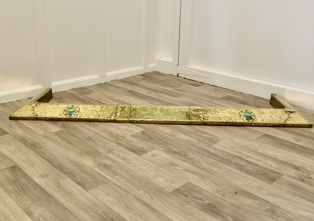 A low hand-hammered brass fireplace fender with riveted joins and two set circular green cabochons.
