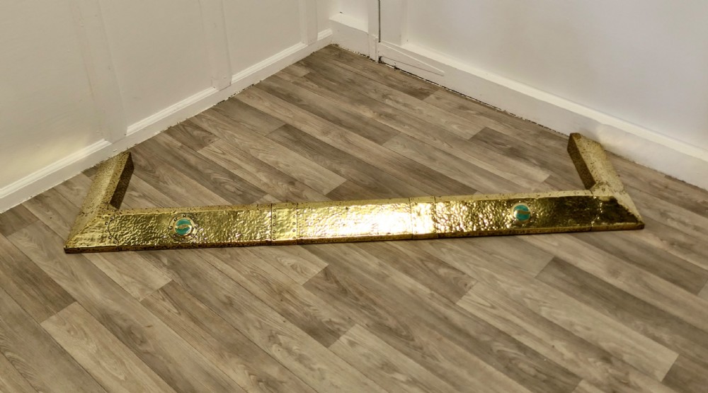 A low hand-hammered brass fireplace fender with riveted joins and two set circular green cabochons. View II