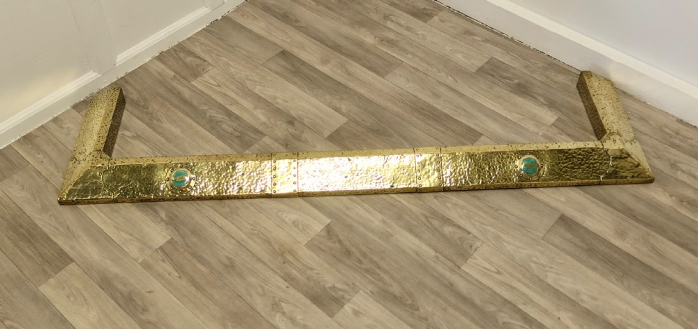 A low hand-hammered brass fireplace fender with riveted joins and two set circular green cabochons. View III