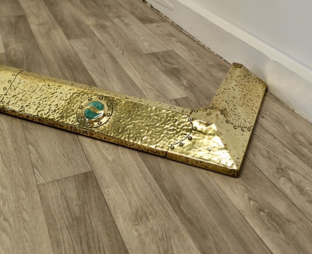 A low hand-hammered brass fireplace fender with riveted joins and two set circular green cabochons. View IV