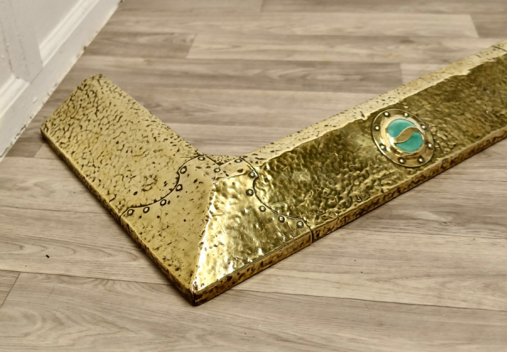 A low hand-hammered brass fireplace fender with riveted joins and two set circular green cabochons. View V