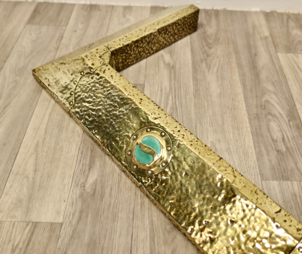 A low hand-hammered brass fireplace fender with riveted joins and two set circular green cabochons. View VI