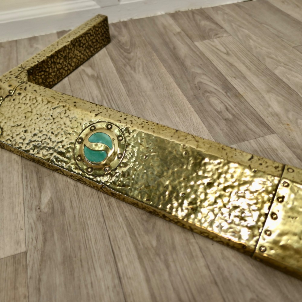 A low hand-hammered brass fireplace fender with riveted joins and two set circular green cabochons. View VII