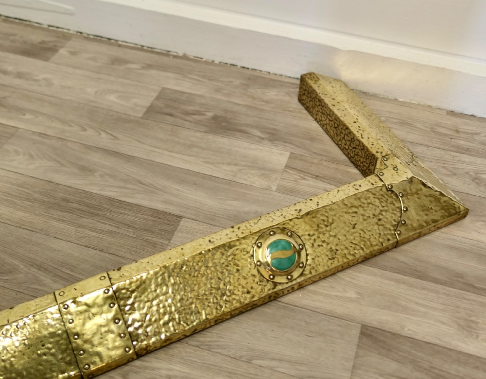 A low hand-hammered brass fireplace fender with riveted joins and two set circular green cabochons. View VIII