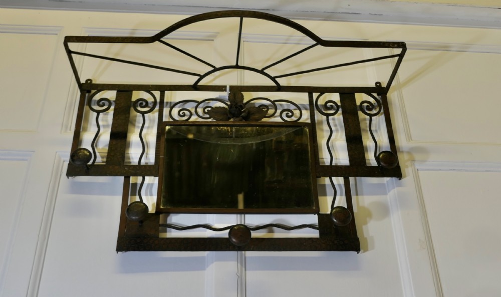 A French Art Deco dark wrought iron wall-mounted rack featuring a central rectangular mirror, top hat shelf, decorative scrollwork, and five coat pegs. View II