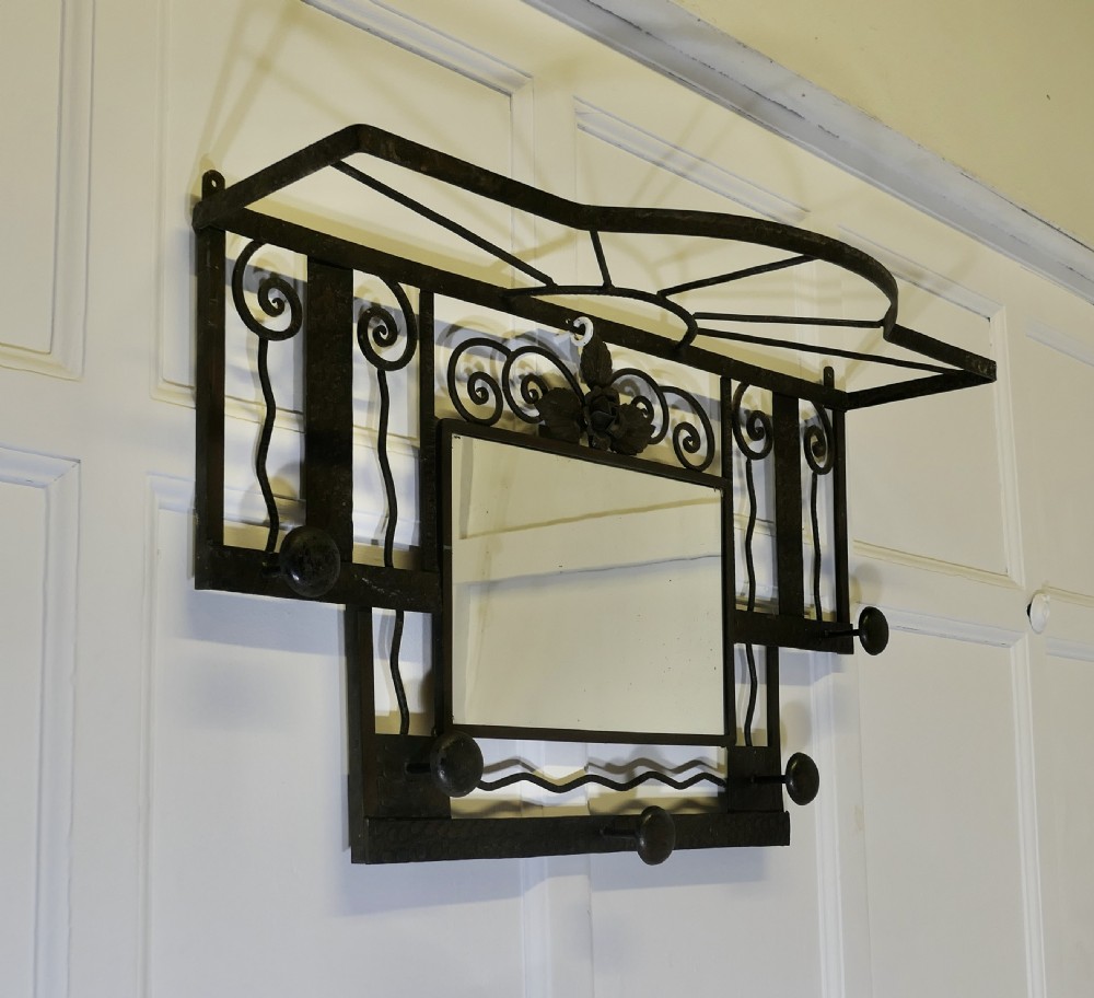 A French Art Deco dark wrought iron wall-mounted rack featuring a central rectangular mirror, top hat shelf, decorative scrollwork, and five coat pegs. View III