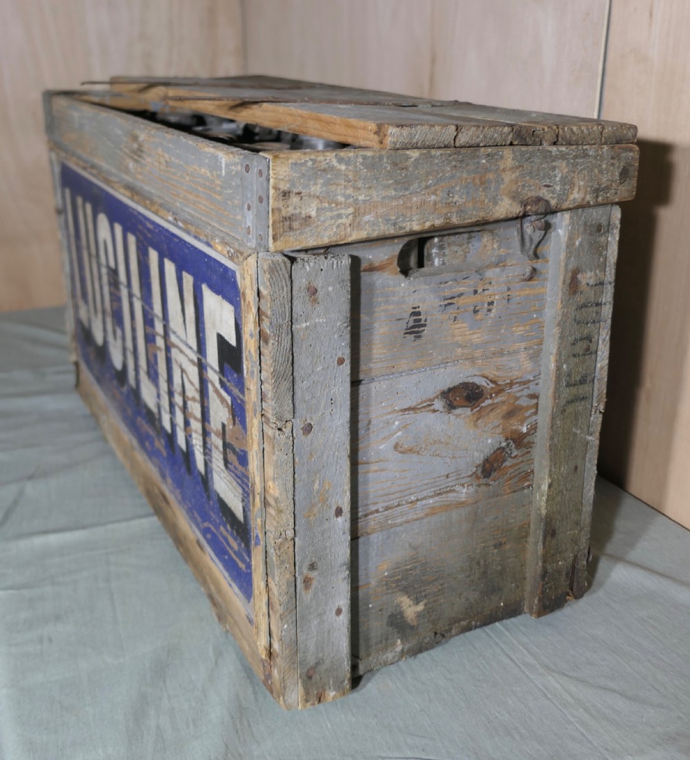 A rectangular weathered wooden shipping crate featuring painted blue typography spelling Luciline across the front panel with metal edge reinforcements. View III