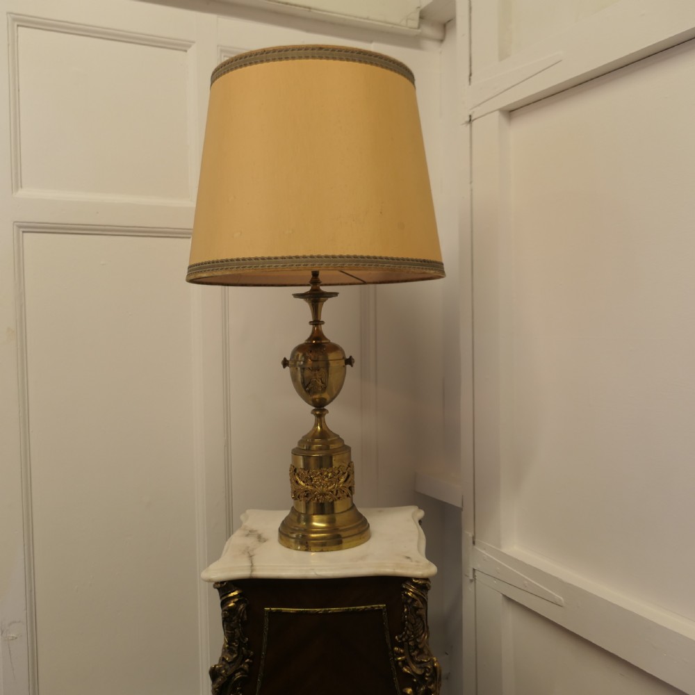 An antique Neoclassical brass table lamp featuring an urn-shaped stem, classical mask reliefs around the base, and a gold fabric shade. View III