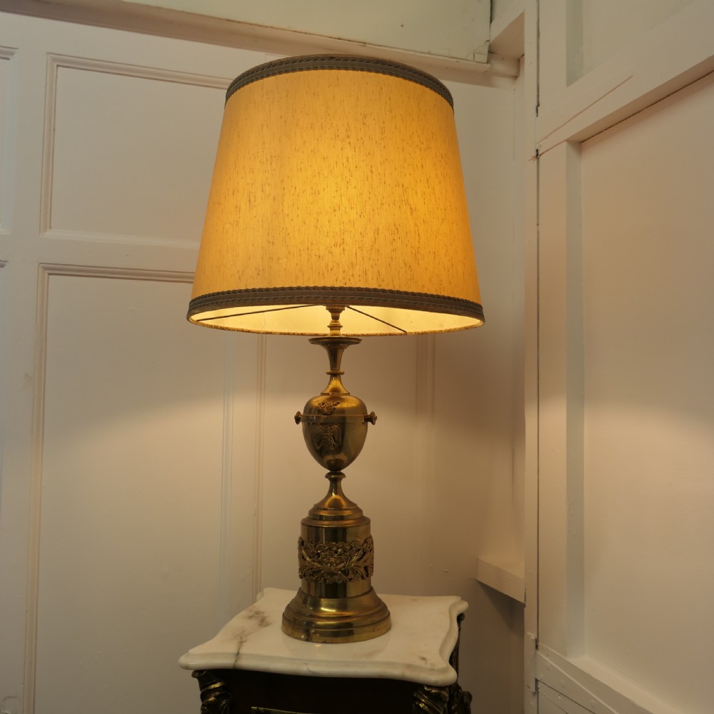 An antique Neoclassical brass table lamp featuring an urn-shaped stem, classical mask reliefs around the base, and a gold fabric shade. View IV