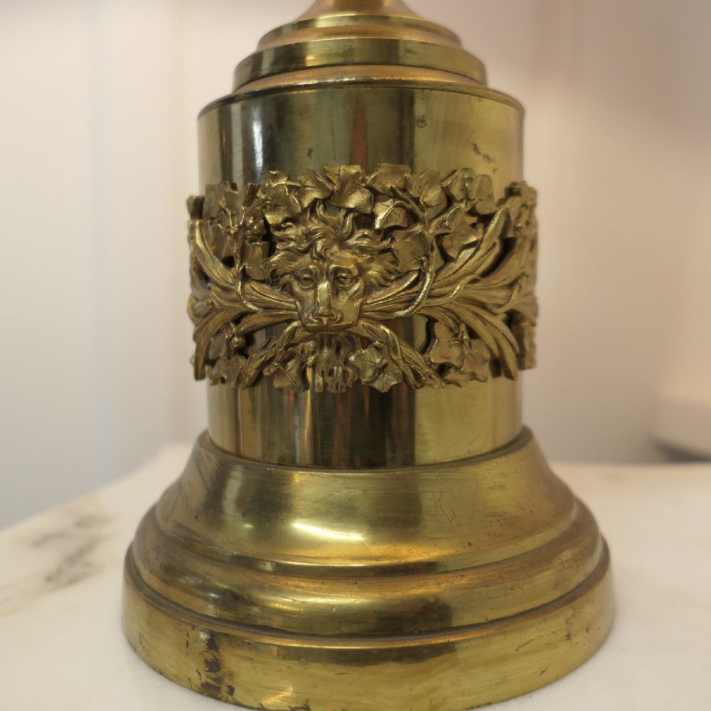 An antique Neoclassical brass table lamp featuring an urn-shaped stem, classical mask reliefs around the base, and a gold fabric shade. View VI