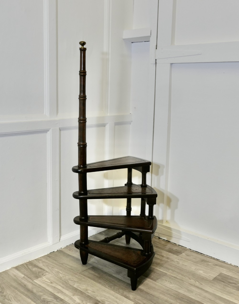 Antique dark wood spiral library steps with four leather-inset treads, turned spindle supports, and a tall central pole capped with a brass finial.