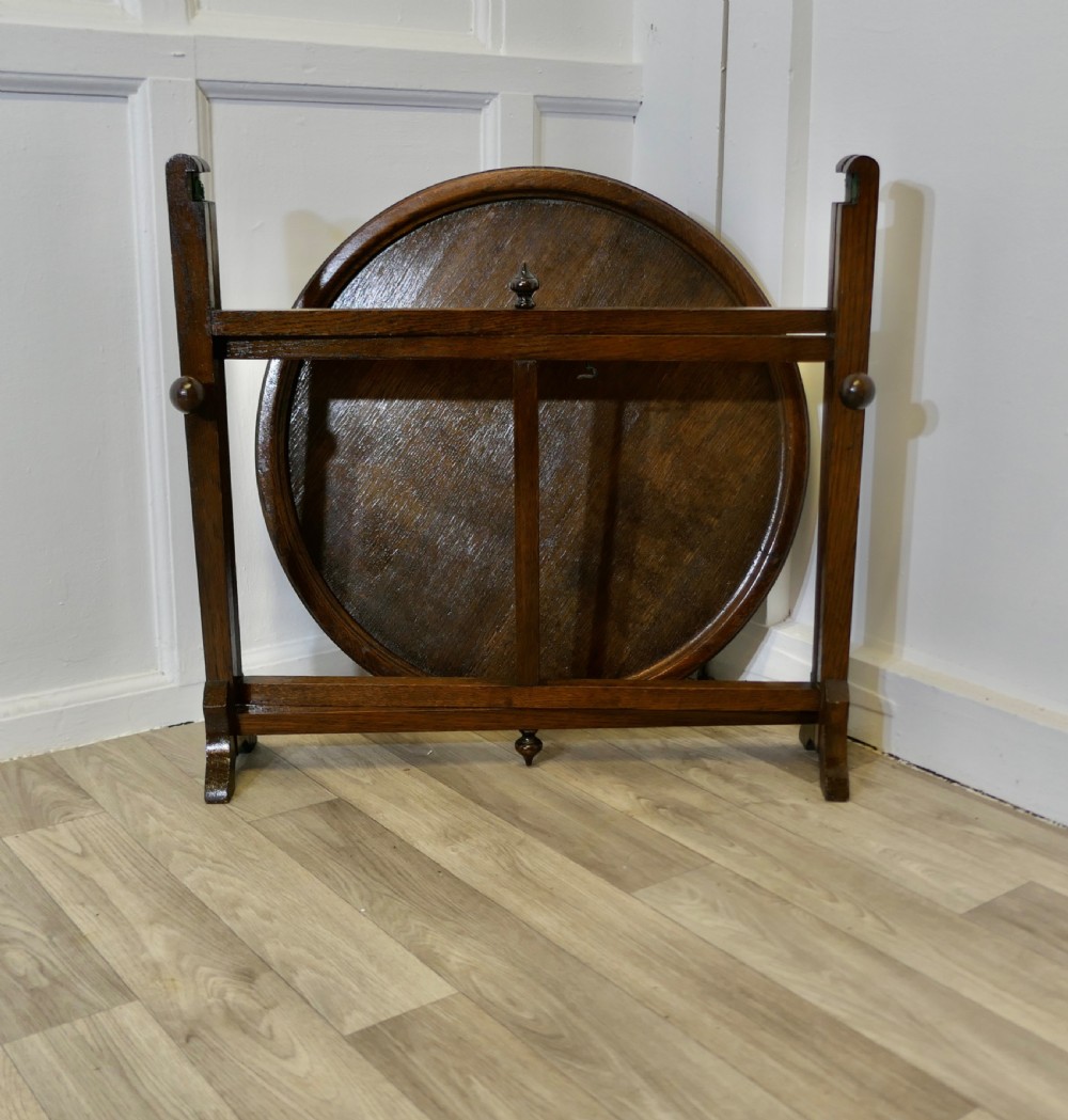 An antique dark oak folding coaching table featuring a circular top mounted on a hinged timber frame.