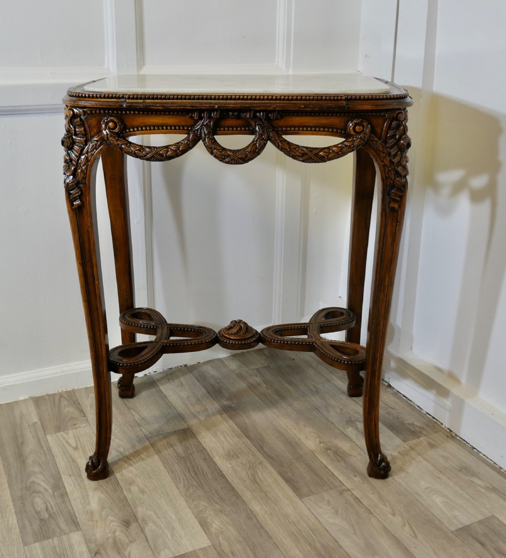 A French carved wooden lamp table featuring a white marble top, sculpted floral garlands, and slender curved legs connected by an ornate stretcher.