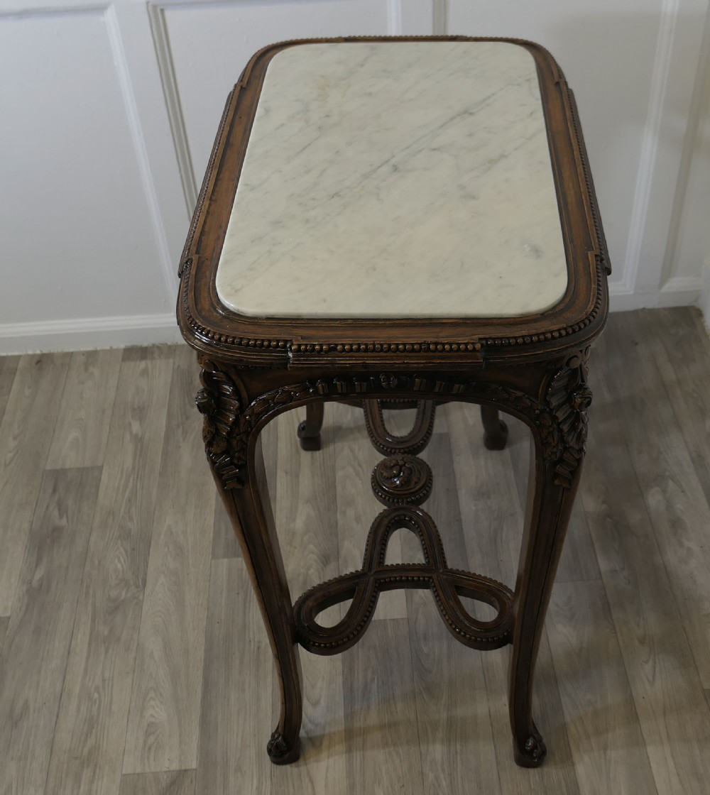 A French carved wooden lamp table featuring a white marble top, sculpted floral garlands, and slender curved legs connected by an ornate stretcher. View VII