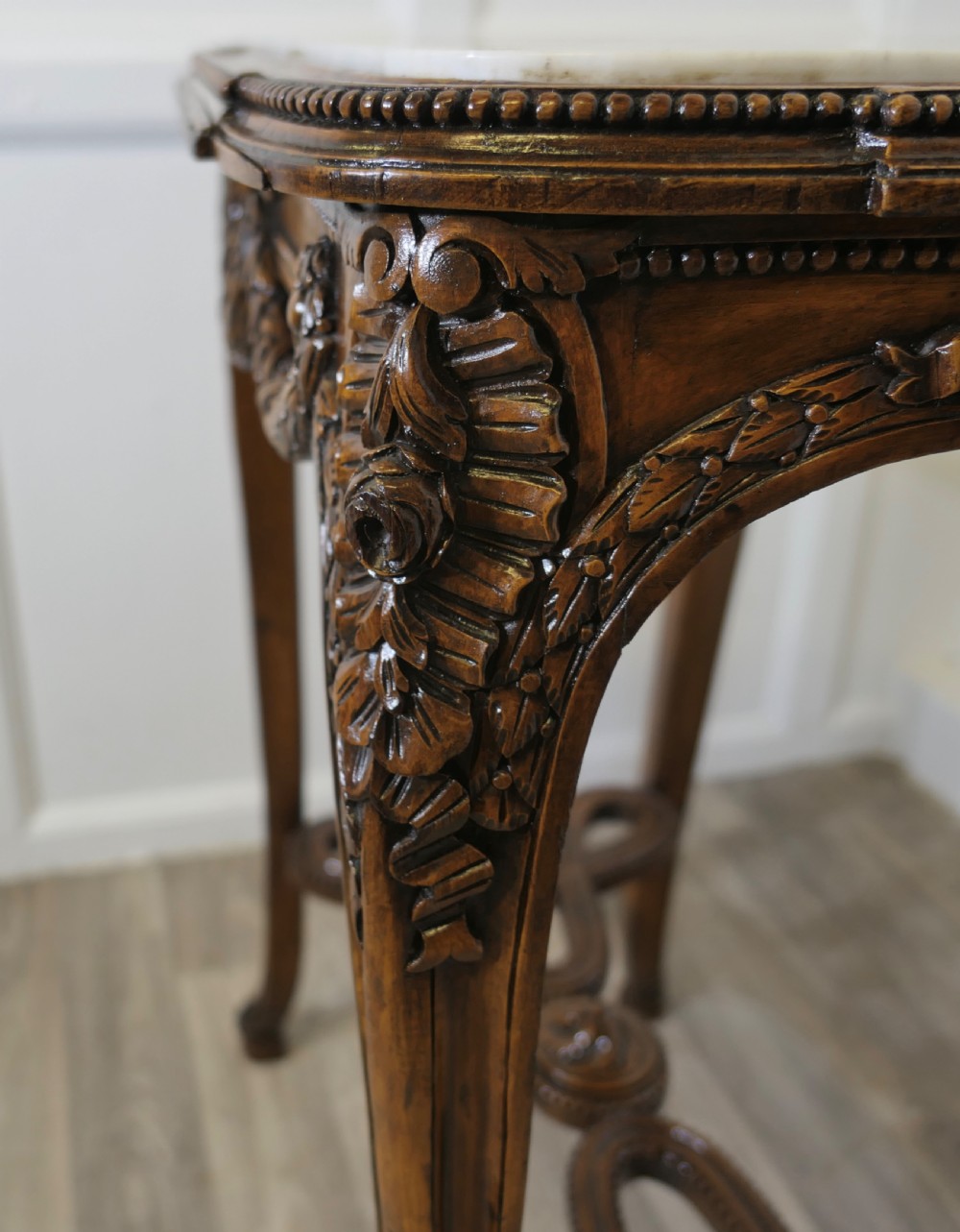 A French carved wooden lamp table featuring a white marble top, sculpted floral garlands, and slender curved legs connected by an ornate stretcher. View IX